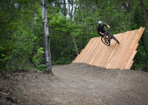 A mountain biker performs a trick on a wooden ramp in a forested area.
