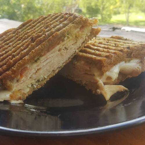 A close-up of a grilled sandwich cut in half, showing layers of cheese and filling on a black plate.