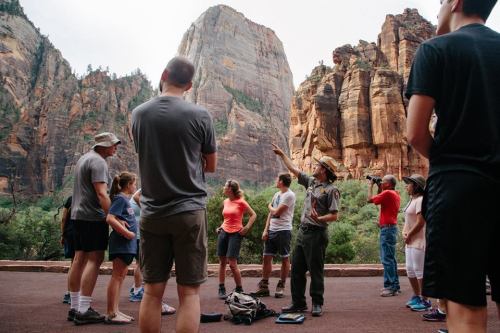 A park ranger leads a group of visitors in a scenic area, surrounded by towering rock formations in a national park.