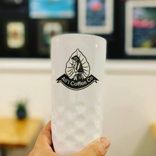A frosted glass with the logo of Alri Coffee Co., set against a blurred background of a café.