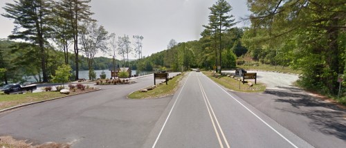 A scenic view of a road leading to a lake, surrounded by trees and parking areas on either side.