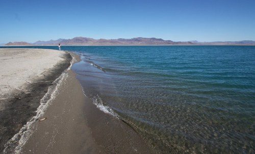 A serene beach with gentle waves lapping at the shore, leading to distant mountains under a clear blue sky.