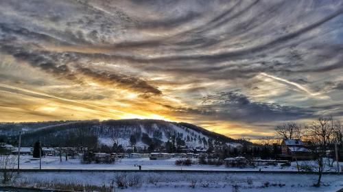 A scenic winter landscape featuring a sunset over snow-covered hills and a cloudy sky.