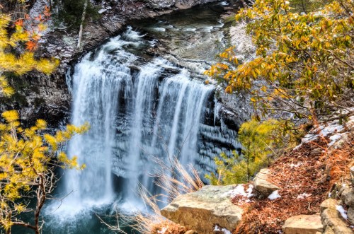 A cascading waterfall surrounded by rocky cliffs and autumn foliage, with a serene pool at the base.