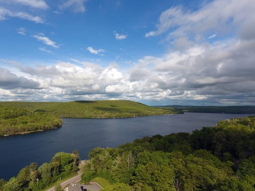 A scenic view of a lake surrounded by lush green hills and a cloudy blue sky.