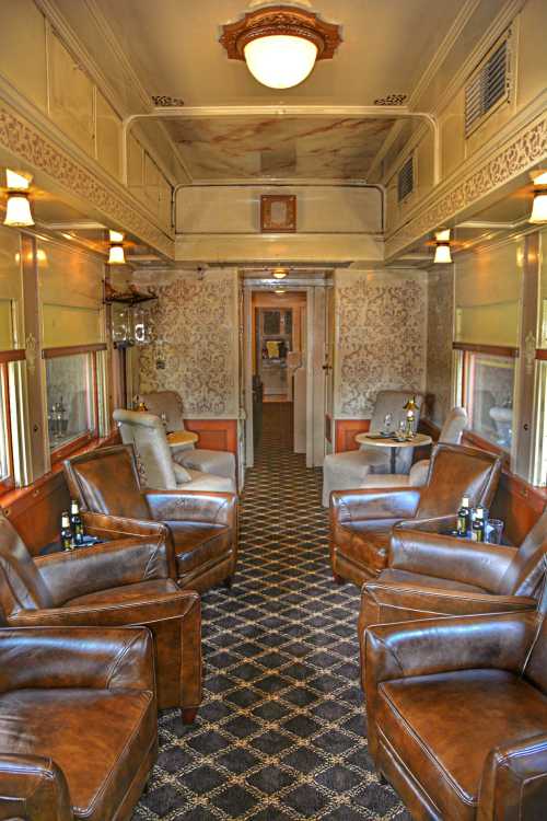 Interior of a vintage train car featuring leather chairs, patterned walls, and a cozy, elegant atmosphere.