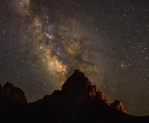A starry night sky with the Milky Way above silhouetted mountain peaks.