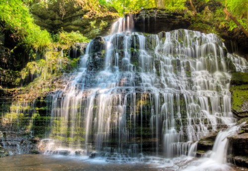 A serene waterfall cascading over rocky cliffs, surrounded by lush green foliage and a tranquil pool below.