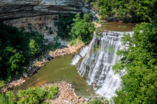 A scenic waterfall cascades into a serene pool, surrounded by lush greenery and rocky cliffs.