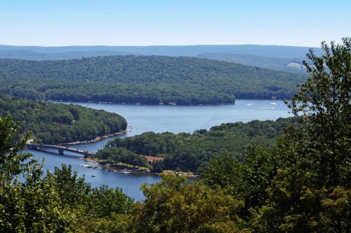 A scenic view of a lake surrounded by lush green hills under a clear blue sky.