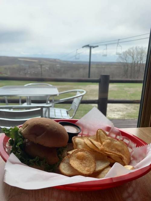 A burger with lettuce and a side of potato chips on a red tray, with a scenic view of mountains and ski lifts in the background.