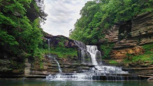 A serene waterfall cascading over rocky cliffs, surrounded by lush green trees and a calm pool below.