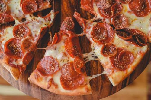A close-up of a pepperoni pizza on a wooden board, with melted cheese and spices visible.