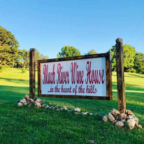 Sign for Black River Wine House, featuring red text on a white background, surrounded by greenery and rocks.