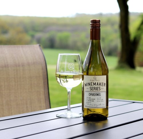 A bottle of Chardonnay and a glass of wine on a table, with a scenic green landscape in the background.
