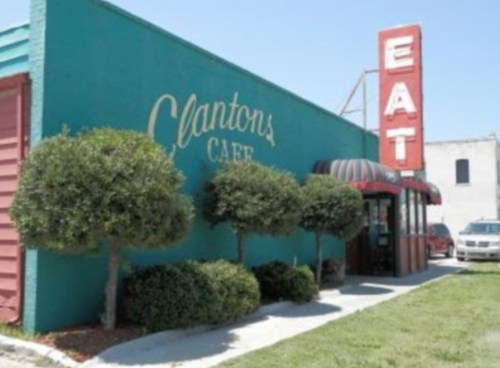 Exterior of Clanton's Cafe with a bright blue wall, trimmed bushes, and a large red "EAT" sign.