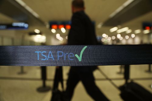 A blurred figure walks past a TSA Pre✓ sign at an airport security checkpoint.