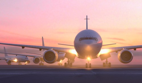 Airplanes lined up on a runway at sunset, with warm colors illuminating the scene.
