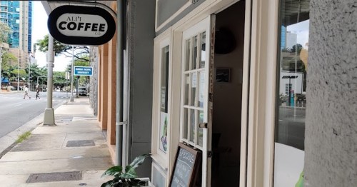 A coffee shop entrance with a sign reading "Ali'i Coffee" and a sidewalk view of the street.