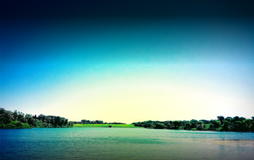 A serene landscape featuring a calm river surrounded by lush greenery under a clear blue sky.