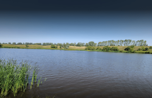 A serene river scene with lush green banks and trees under a clear blue sky.