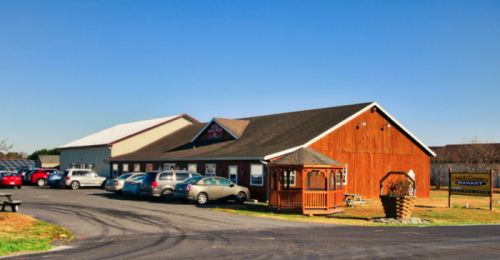 A wooden building with a gazebo, surrounded by parked cars and clear blue skies.