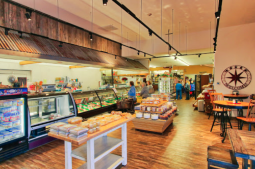 A cozy deli interior with display cases, shelves of baked goods, and customers interacting in a warm atmosphere.