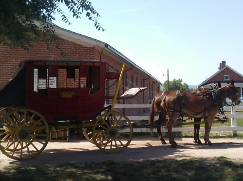 A horse-drawn stagecoach parked beside a historic brick building on a sunny day.