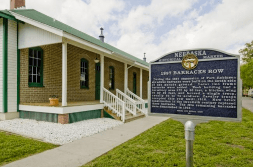Historical marker for 1887 Barracks Row at Fort Robinson, with a brick building and landscaped area in the background.