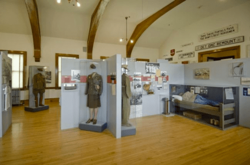 A museum exhibit featuring military uniforms, historical photos, and artifacts in a spacious, well-lit room.