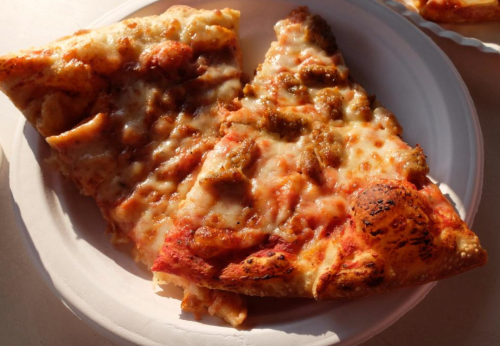 Two slices of cheesy pizza with sausage toppings on a white paper plate.