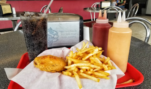 A tray with a drink, fries, and a fried food item, set on a table in a casual dining environment.