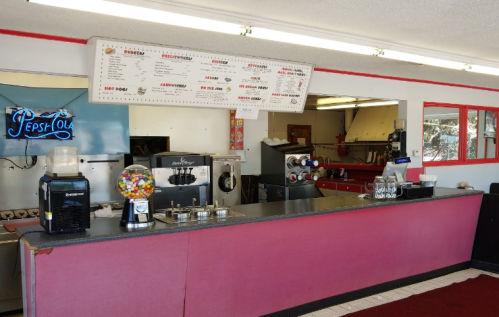 A colorful diner counter with a menu board, soda fountain, and candy dispenser in a bright, retro setting.