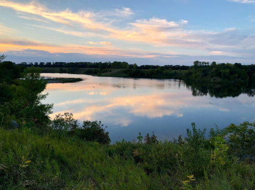A serene river scene at sunset, reflecting colorful clouds and surrounded by lush greenery.