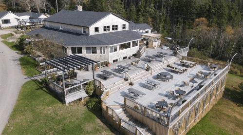 Aerial view of a large building with outdoor seating areas and wooden decks surrounded by trees.