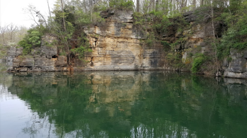 A serene lake surrounded by rocky cliffs and lush greenery, reflecting the landscape in calm waters.