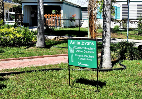 A green sign in a yard reads "Anita Evans, Certified Medium, Spiritual Counselor, Private & Telephone Consultations."