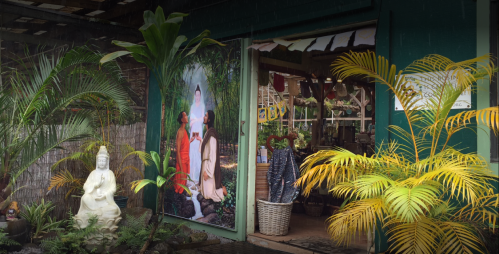 A serene outdoor space with lush plants, a statue, and a large mural depicting two people in a tranquil setting.