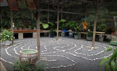 A serene indoor space featuring a stone labyrinth surrounded by plants and decorative elements.