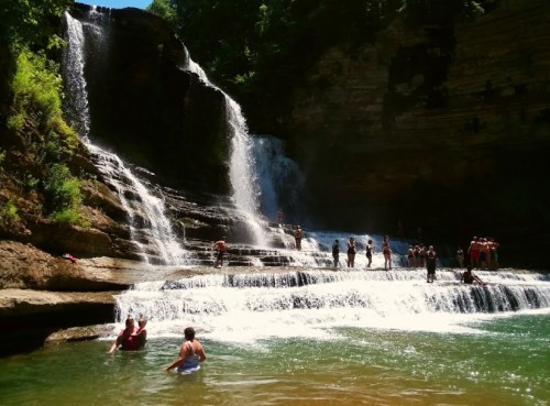 A scenic waterfall with people swimming and enjoying the water in a lush, green environment.