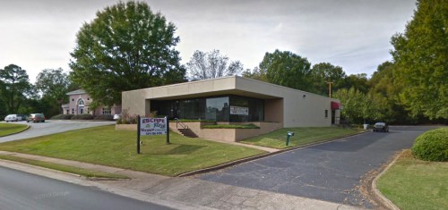 A modern building with large windows, surrounded by trees and a parking area, featuring a sign for "ESCAPE."