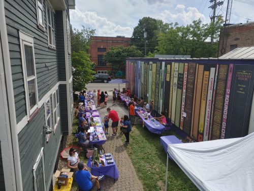Aerial view of a community event with tables, people, and a colorful mural of books on a building.