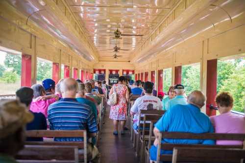 Interior of a vintage train car filled with passengers, some seated and others standing, enjoying a scenic ride.