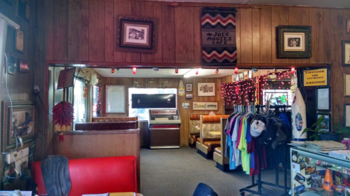 Cozy diner interior with wooden walls, vintage decor, a jukebox, and colorful clothing displayed on racks.