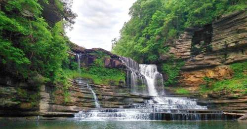 A serene waterfall cascading over rocky cliffs, surrounded by lush green trees and a calm pool of water below.