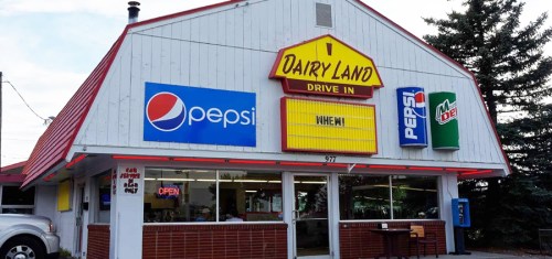 A retro drive-in restaurant with a red roof, featuring Pepsi signage and an "Open" sign in the window.