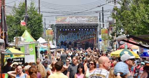 A bustling music festival scene with a crowd enjoying performances, food trucks, and colorful banners in the background.