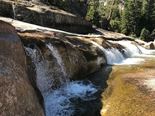 A serene waterfall cascading over smooth rocks, surrounded by lush green trees in a natural setting.
