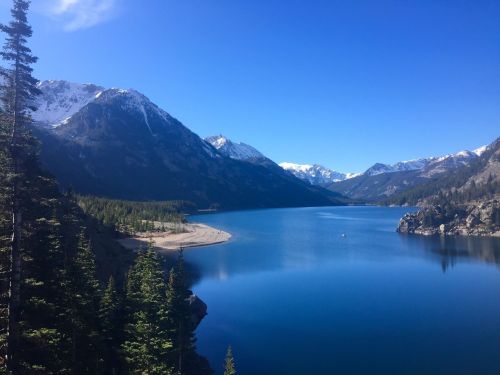 A serene lake surrounded by mountains, with clear blue skies and a sandy beach along the shore.
