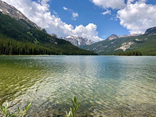 A serene lake surrounded by mountains and lush forests under a partly cloudy sky.